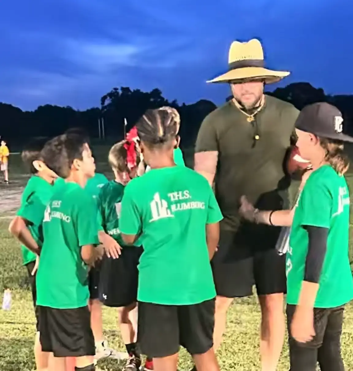 Coach addressing youth team on field at dusk
